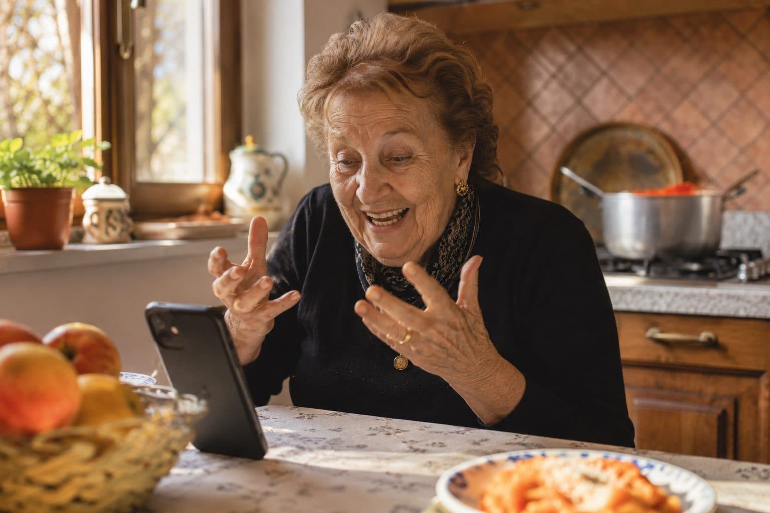 Una nonna ride parlando al telefono appoggiato sul tavolo di cucina, con la pentola del sugo sul fuoco alle spalle